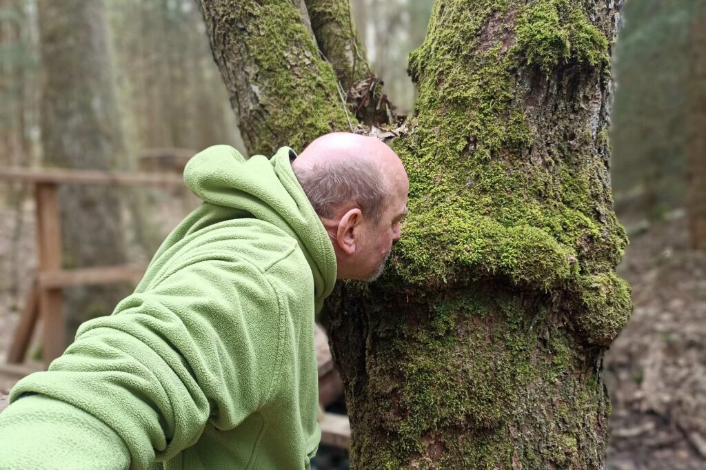 Thomas Nawroth betrachtet Moos an einem Baum im Wald