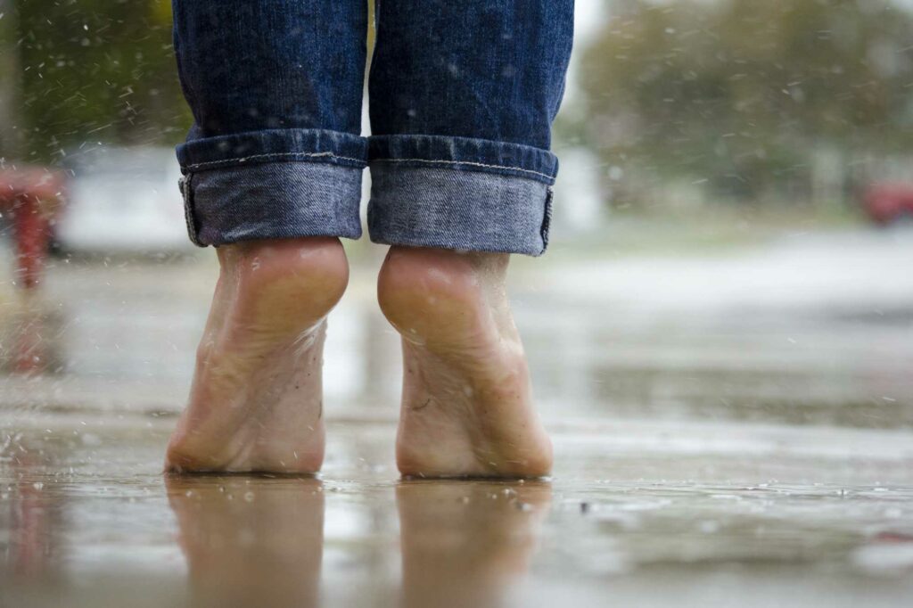 Eine Person steht barfuß auf regennasser Straße auf den Zehenspitzen