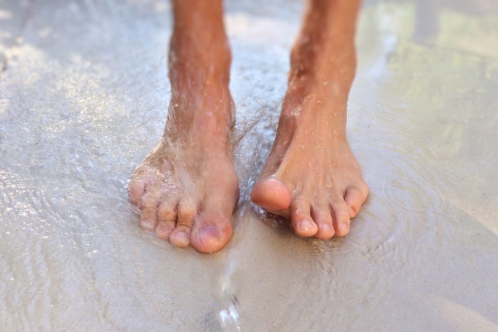 Aufnahme von nackten Füßen im Wasser am Sandstrand