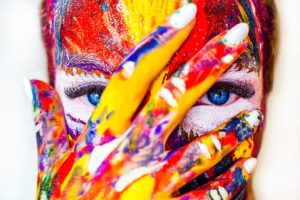 Bodypainting - eine Frau hält die Hand vor ihr Gesicht. Beides ist bunt bemalt